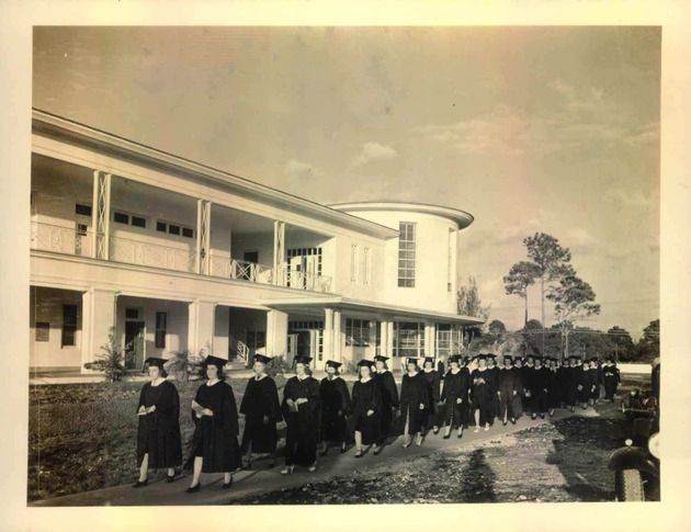 Students wearing their formal academic attire walk in procession in front of Adrian Hall